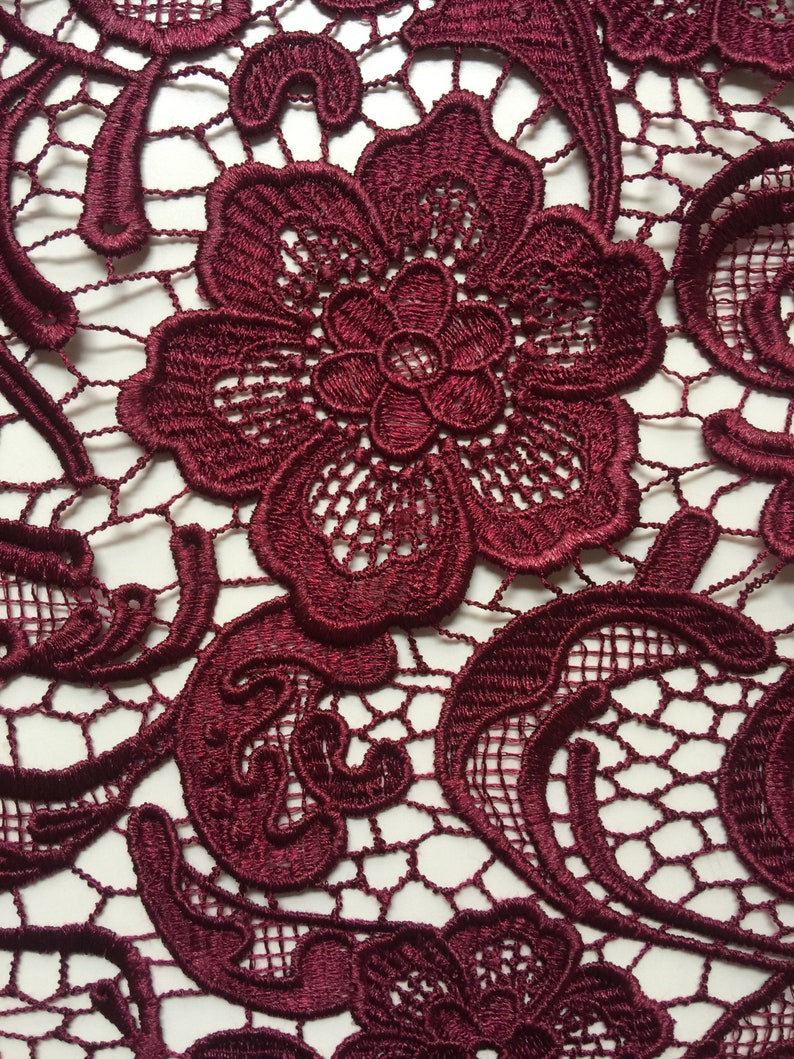 May include: Burgundy lace fabric with a delicate floral pattern. The lace is intricate and detailed, with a fine mesh background.