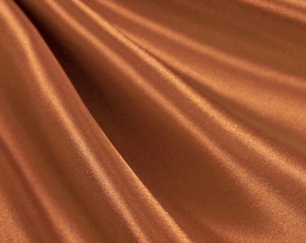 Op de afbeelding: Close-up van een vloeiende, koperkleurige satijnen stof. De stof is gedrapeerd, waardoor zachte plooien en highlights ontstaan. De satijn heeft een subtiele glans, die het licht reflecteert en diepte aan de afbeelding toevoegt. Het algehele effect is er een van luxe en elegantie.