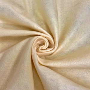 May include: A close-up of a soft, pale peach-colored fabric. The fabric is folded and draped, creating a smooth, flowing texture.