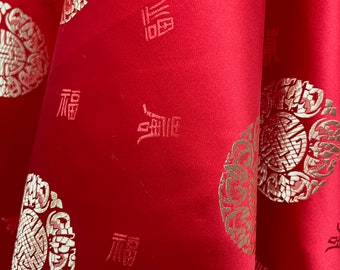Könnte beinhalten: Roter Stoff mit einem goldenen Stickmuster. Das Muster enthält ein sich wiederholendes Design eines Kreises mit einer stilisierten Blume im Inneren und das chinesische Schriftzeichen für "Glück" in Gold.
