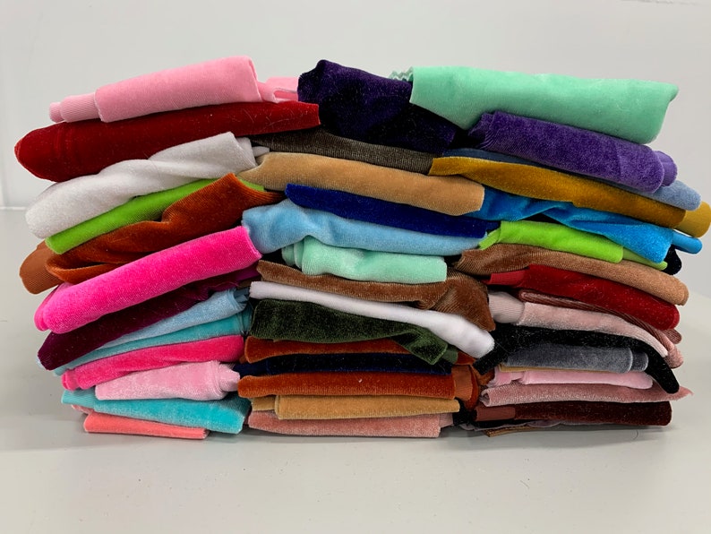 K&ouml;nnte beinhalten: Ein Stapel bunter Samtstoffmuster in verschiedenen Farbt&ouml;nen von Rosa, Gr&uuml;n, Blau, Braun, Rot und Wei&szlig;.