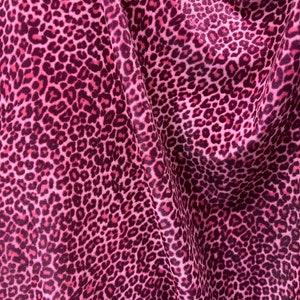 May include: Pink fabric with a leopard print pattern. The fabric is soft and has a slight sheen.