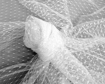 May include: A roll of white dotted tulle fabric. The tulle is soft and delicate, with a fine mesh and small, evenly spaced dots. The fabric is draped and folded, creating a sense of texture and depth. Ideal for bridal veils, dresses, or craft projects.