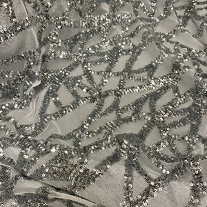 May include: Silver sequined fabric with a geometric pattern on a sheer mesh base. The sequins are small and closely spaced, creating a shimmering effect.