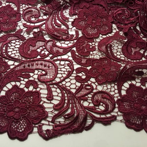 May include: Burgundy lace fabric with a floral pattern. The lace has a delicate, intricate design with small flowers and swirls.