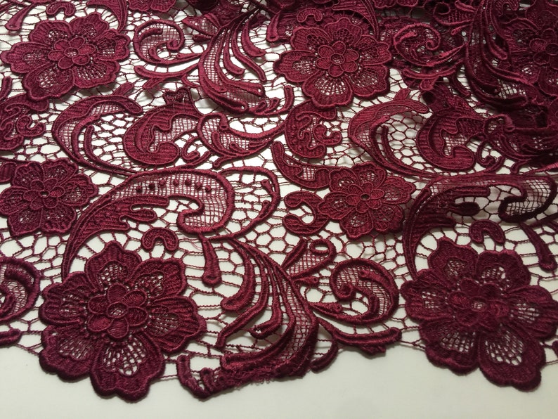 May include: Burgundy lace fabric with a floral pattern. The lace has a delicate, intricate design with small flowers and swirls.