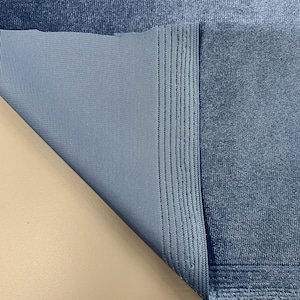 May include: Close-up of a blue fabric with a textured surface. The fabric is folded over, revealing a smooth, woven backing. A measuring tape is visible at the bottom of the image, showing measurements in inches.
