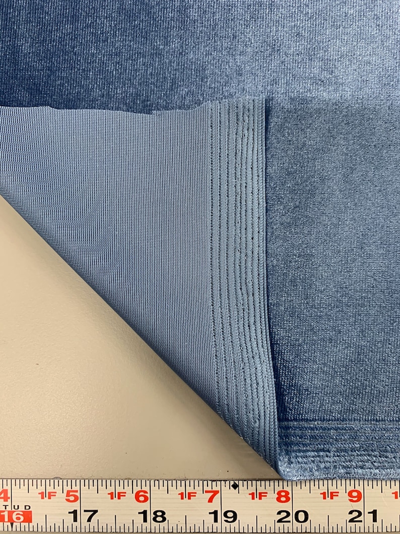 May include: Close-up of a blue fabric with a textured surface. The fabric is folded over, revealing a smooth, woven backing. A measuring tape is visible at the bottom of the image, showing measurements in inches.