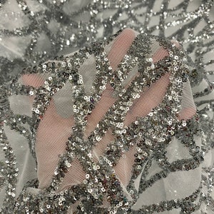 May include: Silver sequin fabric with a white mesh backing. The sequins are arranged in a geometric pattern.