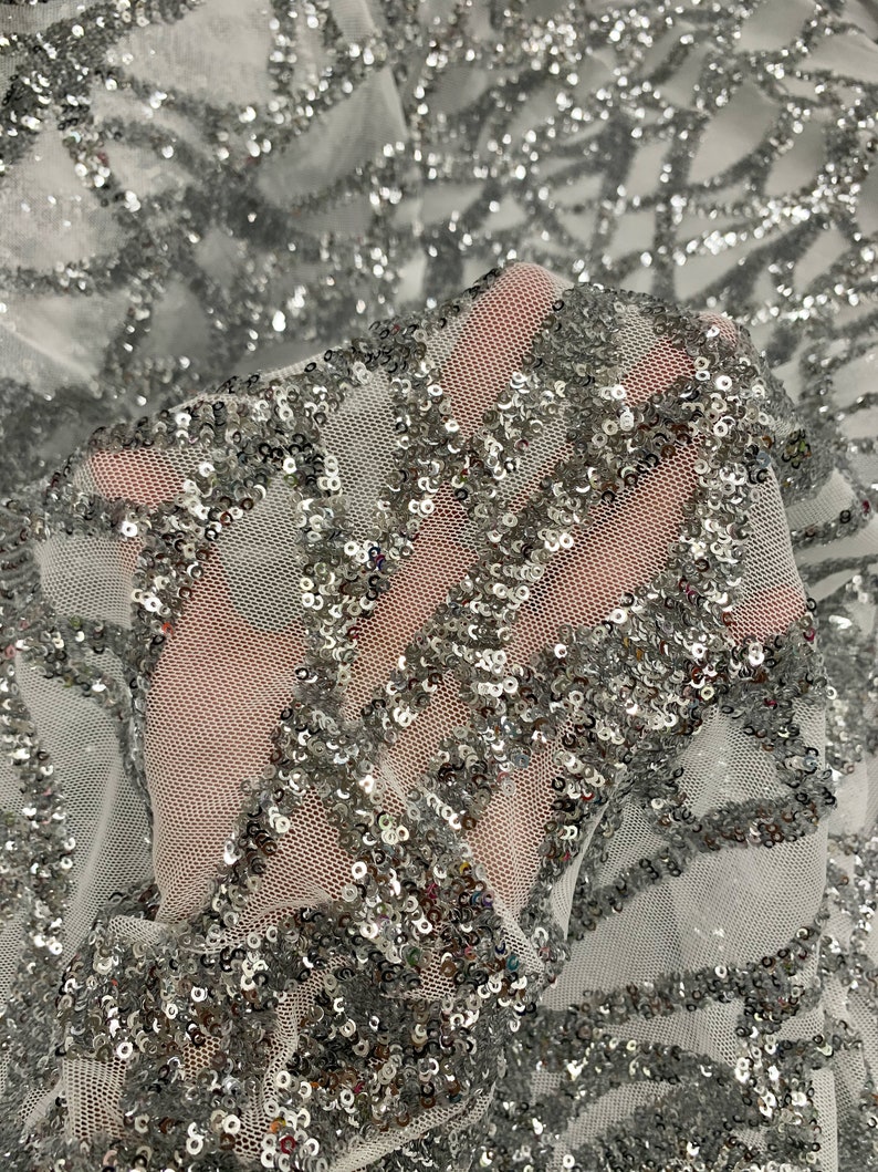 May include: Silver sequin fabric with a white mesh backing. The sequins are arranged in a geometric pattern.