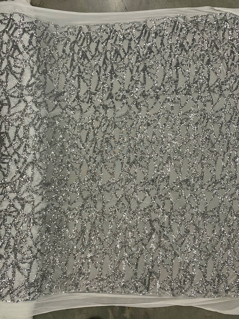May include: Silver glitter fabric with a geometric pattern. The fabric has a mesh backing.