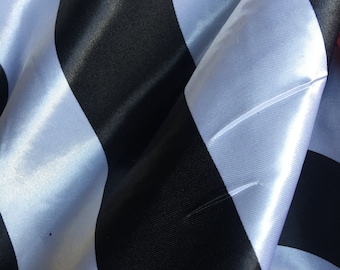 May include: Black and white striped fabric with a satin finish. The fabric is folded and draped, creating a textured look.