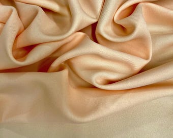 Puede incluir: Primer plano de tela color melocotón con pliegues suaves y un brillo sutil. El material parece suave y lujoso, con un degradado de color de melocotón claro a un tono más profundo y cálido. La tela probablemente se utiliza para ropa o decoración del hogar.