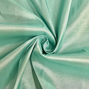 May include: A close-up of a smooth, silky fabric in a light teal green color. The fabric is draped and folded, showcasing its texture and sheen.