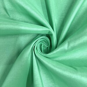 May include: A close-up of a smooth, light green fabric with a silky sheen. The fabric is folded and draped, creating a soft, flowing texture.