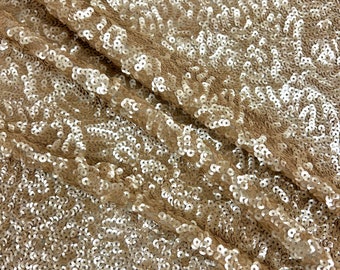 May include: A close-up of a fabric with a shimmering gold sequin pattern. The sequins are small and round, and they are arranged in a random pattern. The fabric is soft and flexible, and it has a luxurious feel.