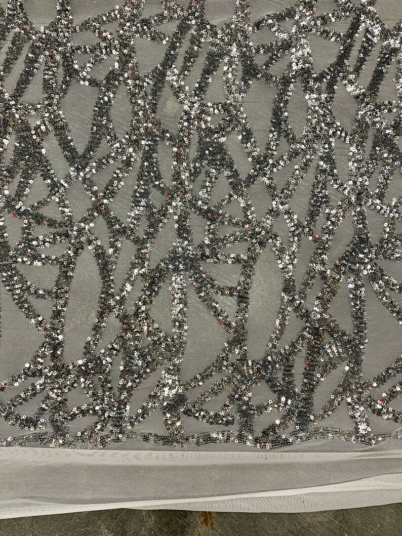 May include: Silver sequined fabric with a geometric pattern on a white mesh background.