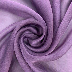 May include: A close-up of a soft, purple fabric with a smooth, silky texture. The fabric is draped and folded, creating a swirling pattern.