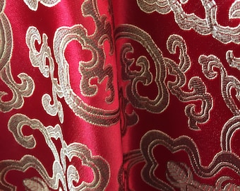 Könnte beinhalten: Roter Stoff mit einem goldenen und braunen Brokatmuster. Das Muster zeigt wirbelnde Designs und florale Motive.