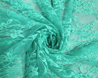 Pode incluir: Close-up de um tecido de renda turquesa com um padrão floral. O tecido é reunido e rodopiado, criando um efeito texturizado. A renda é delicada e semi-transparente, com um brilho subtil.