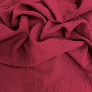 May include: Close-up of a deep red fabric with a textured, slightly wrinkled surface. The fabric is draped and folded, creating shadows and highlights that emphasize its texture. The color is a rich, saturated shade of red.