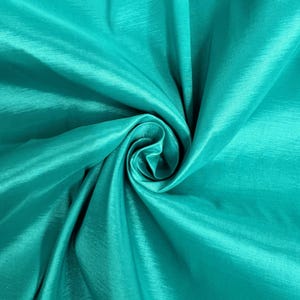 May include: A close-up of teal fabric with a soft, silky texture. The fabric is folded and twisted, creating a swirling pattern.