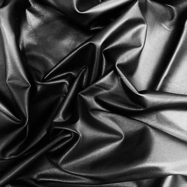 May include: Black faux leather fabric with a smooth, shiny finish. The fabric is draped and folded, creating soft, flowing lines.