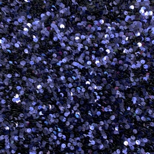 Puede incluir: Primer plano de una tela cubierta de pequeñas lentejuelas azules iridiscentes. Las lentejuelas están muy juntas, creando un efecto brillante.