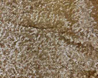 May include: Gold sequin fabric with a sheer mesh backing. The sequins are small and tightly packed, creating a shimmering effect.