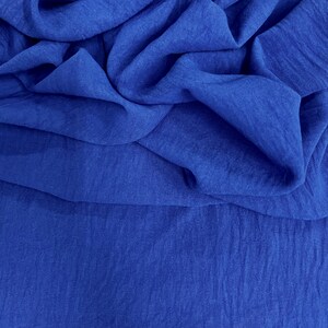 May include: Close-up of a vibrant blue fabric with a textured, crinkled appearance. The fabric is draped and folded, creating shadows and depth. The color is a rich, saturated blue, with subtle variations in tone.