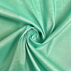 May include: A close-up of a soft, smooth, mint green fabric with a subtle sheen. The fabric is draped and folded, creating a luxurious and elegant look.