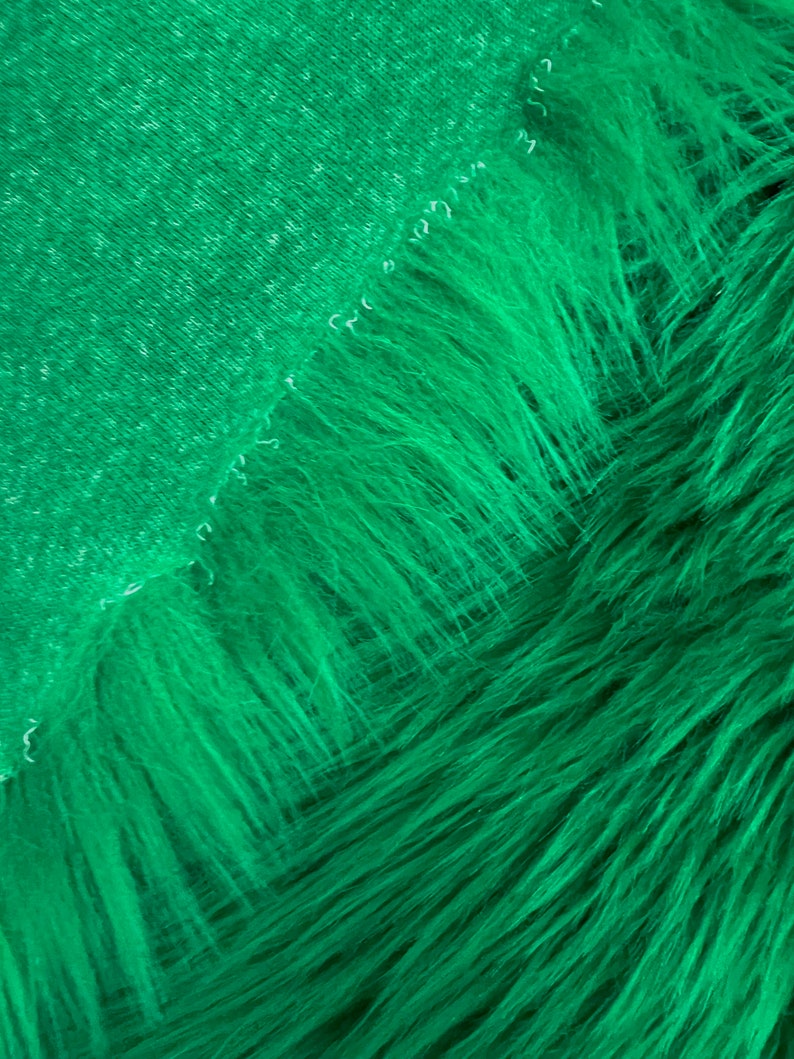 May include: A close-up of a bright green faux fur fabric. The fabric has a soft, plush texture and a subtle sheen.