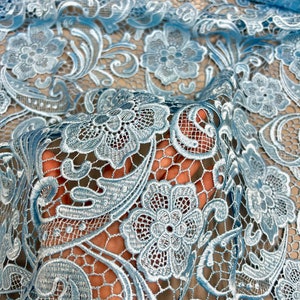 May include: Light blue lace fabric with a delicate floral pattern. The lace is intricate and has a soft, airy feel.