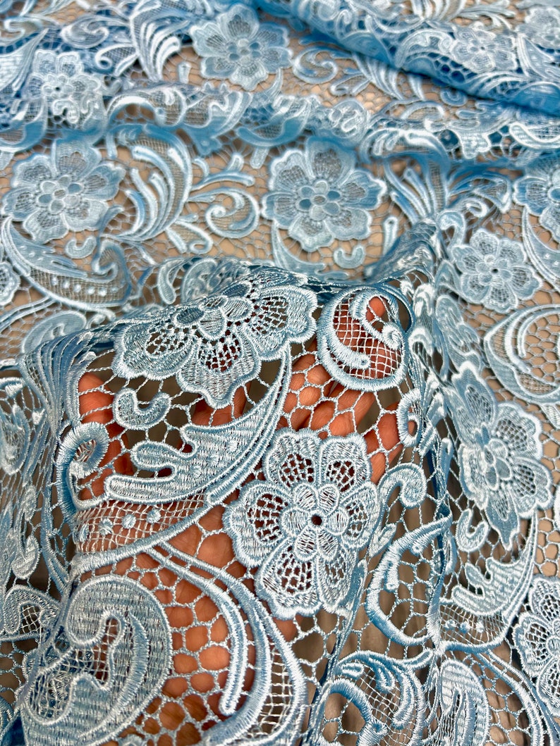 May include: Light blue lace fabric with a delicate floral pattern. The lace is intricate and has a soft, airy feel.