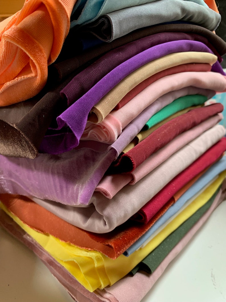 May include: A stack of fabric swatches in various colors and textures, including orange, purple, pink, green, brown, and blue.