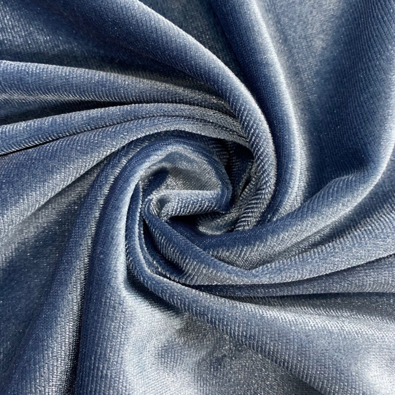 May include: Close-up of a soft, blue velvet fabric with a subtle ribbed texture. The fabric is folded and draped, showcasing its luxurious feel.