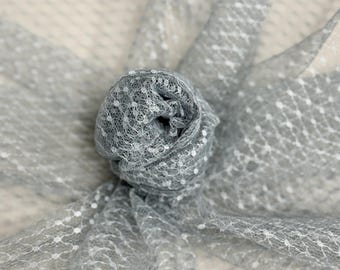 May include: A close-up of a rolled-up, light gray fabric with a delicate, open weave. The fabric is dotted with small, white, evenly spaced accents. The material is soft and appears to be lightweight, suitable for various craft projects.
