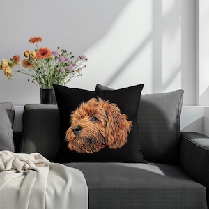 Op de afbeelding: Zwart vierkant sierkussen met een gedetailleerde illustratie van een bruine hondenkop. De vacht van de hond is weergegeven met gloeiende oranje lijnen. Het kussen ligt op een grijze bank.