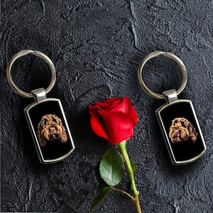 May include: Two silver keychains with black rectangular tags featuring a brown dog's face. A single red rose with green leaves is in the background.