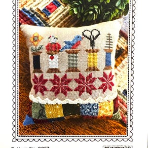 May include: A decorative pillow with embroidered spools, scissors, and a bird. The pillow has a patchwork base and a scalloped border. The text "Tools and Spools" is at the top. The pattern number is 0057.