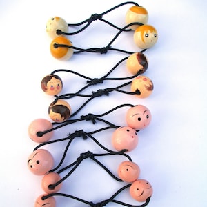 May include: A set of 10 hair ties with wooden beads. The beads are painted with different faces and are in shades of pink, yellow, and brown.
