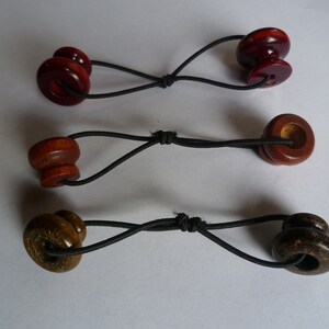 May include: Three wooden hair ties with black elastic bands. The hair ties are in different colors and patterns. The first hair tie is dark red, the second is light brown, and the third is dark brown with a wood grain pattern.