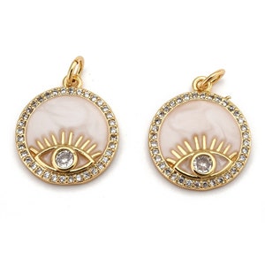 May include: Two gold-tone pendants with a white enamel eye design and clear crystal accents. The pendants are round and have a clear crystal halo around the eye.