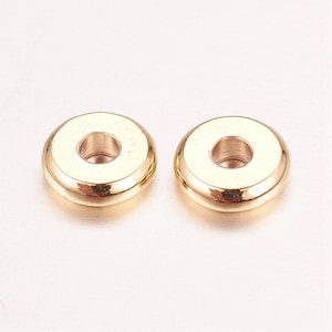 May include: Two gold-colored metal spacer beads with a round shape and a hole in the center.