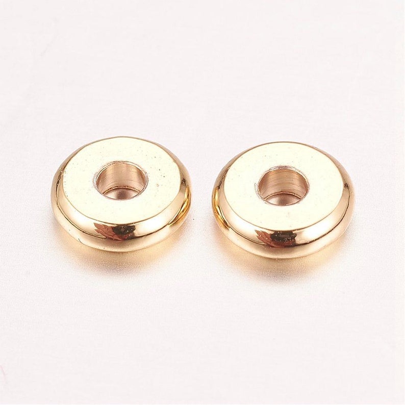 May include: Two gold-colored metal spacer beads with a round shape and a hole in the center.