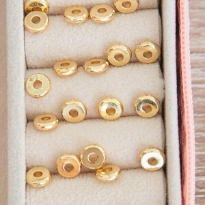 Puede incluir: Primer plano de una caja de joyer&iacute;a rosa con varios compartimentos llenos de anillos de metal dorado. Los anillos est&aacute;n dispuestos en filas y todos son del mismo tama&ntilde;o y forma.