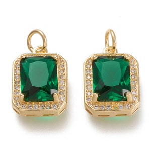 May include: Two gold-tone pendant charms with a square emerald green gemstone surrounded by a halo of smaller clear gemstones.
