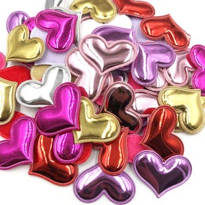 May include: A collection of heart-shaped embellishments in various colors, including gold, silver, pink, red, and purple. The hearts are made of a shiny, metallic material and have a raised, three-dimensional design.