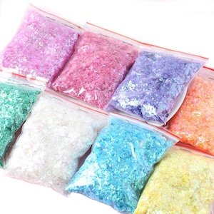 May include: Eight small bags of iridescent glitter flakes in various colours, including pink, purple, blue, green, white, and orange. The bags are clear plastic with red zipper closures.