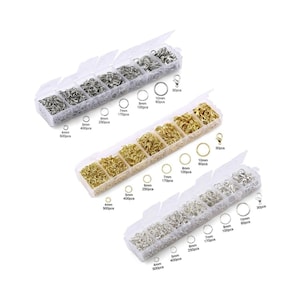 May include: Three clear plastic boxes filled with silver and gold jump rings of various sizes. The boxes are labeled with the size and quantity of each ring. The boxes are arranged in a row from left to right.